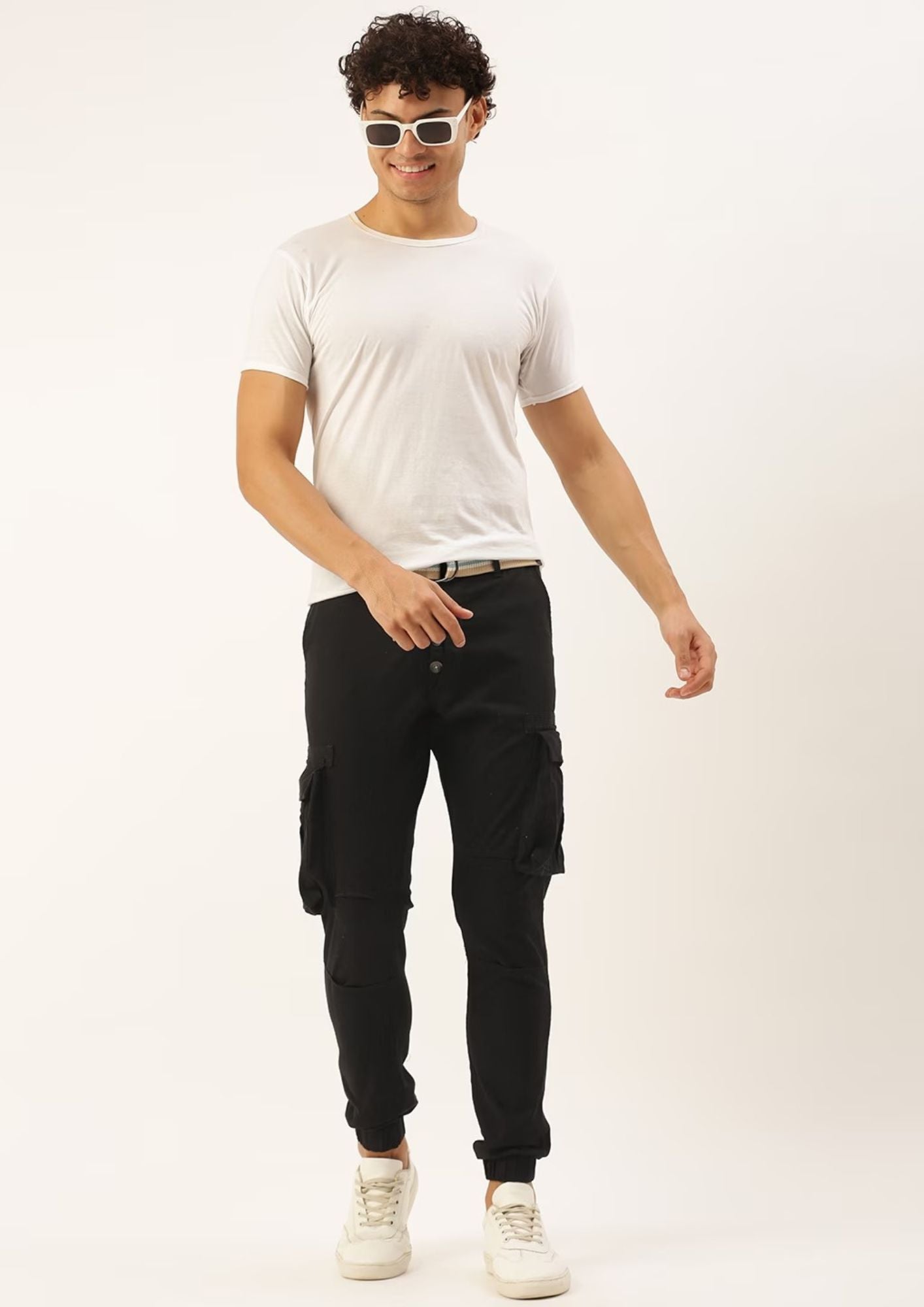 A man wearing sunglasses and a white t-shirt, with black cargo pants and a belt.