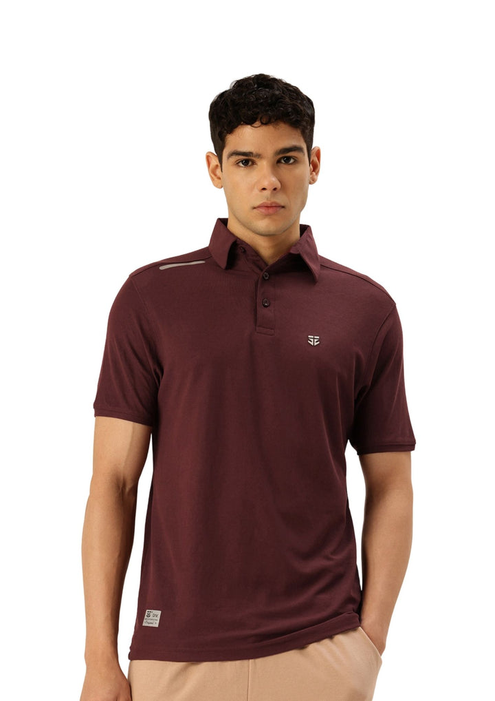 A man wearing a short-sleeve polo shirt in maroon with a small embroidered crest logo on the left chest, photographed against a plain white background.