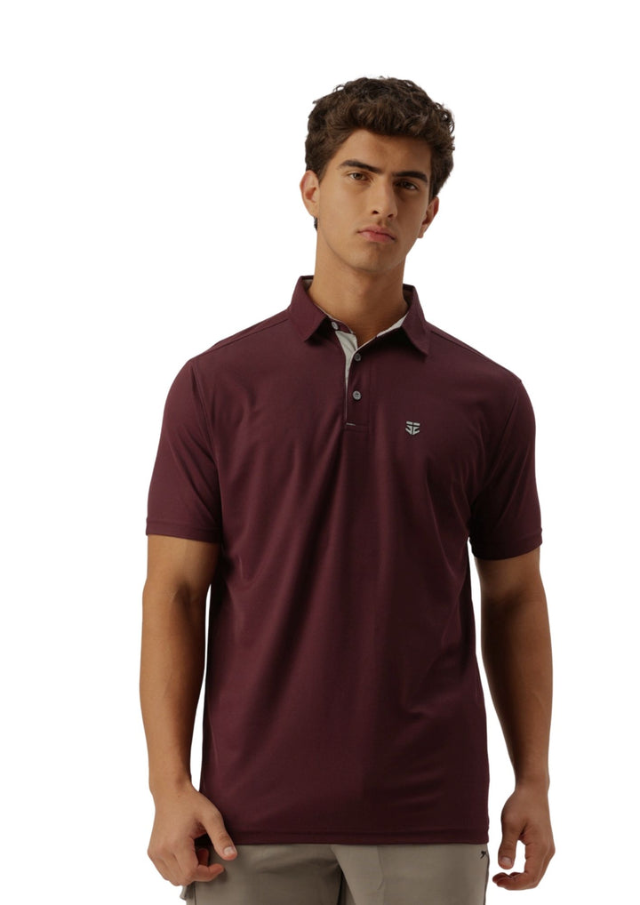 A man wearing a short-sleeve polo shirt in maroon with a small embroidered crest logo on the left chest, paired with light gray trousers, against a plain white background.