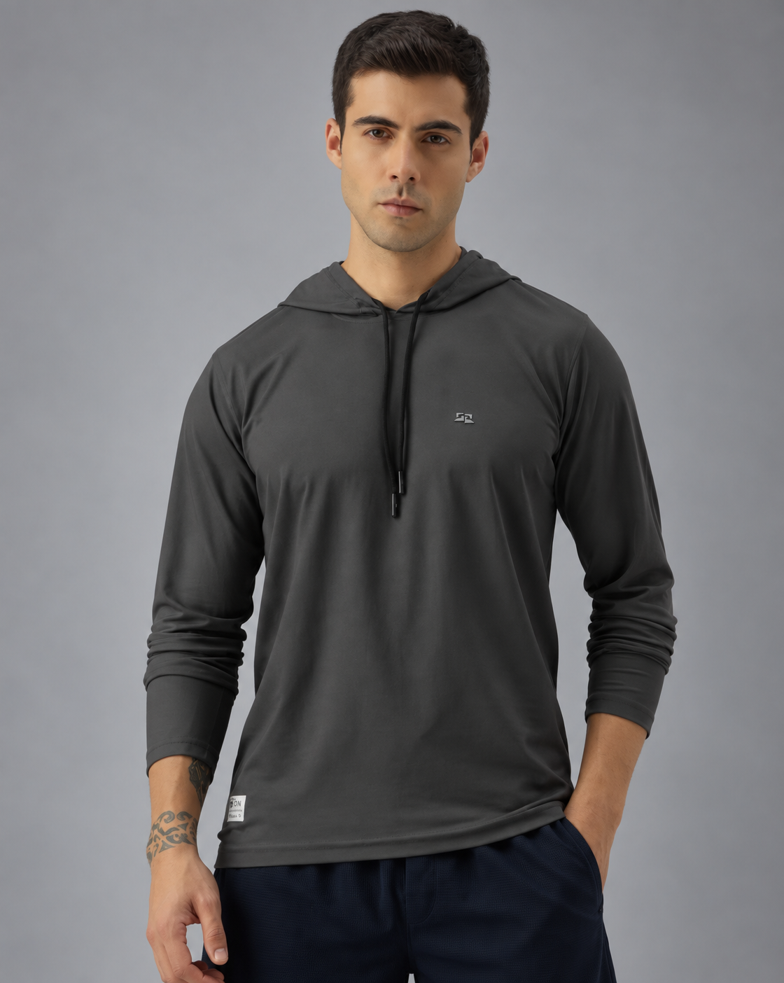 A man wearing a dark gray long-sleeve athletic hoodie with a small white chest logo, photographed against a solid grey background.