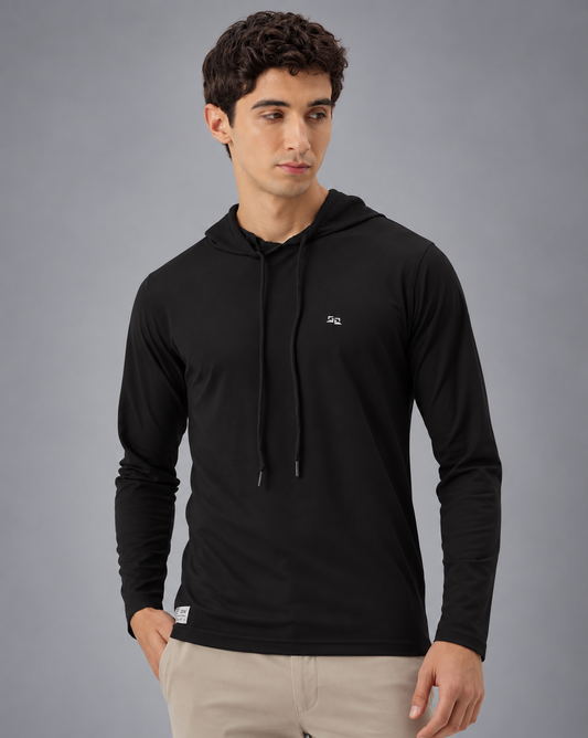 A man wearing a black long-sleeve athletic hoodie with drawstrings and a small white logo on the left chest, paired with light beige pants, against a plain grey background.