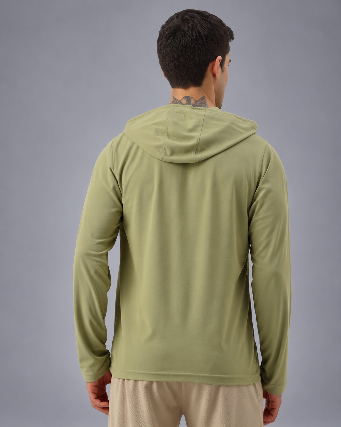 A man viewed from the back wearing a light olive green hooded long-sleeve athletic top and beige pants, set against a solid gray studio background.